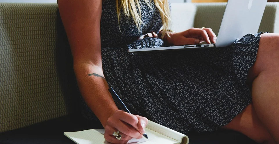 imagem de uma mulher sentada com notebook no colo e caderno ao lado anotando textos como um tradutor juramentado francês